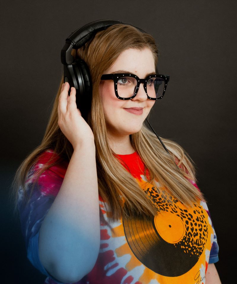 meagan brownrigg from grove betty wearing headphones and thick framed glasses