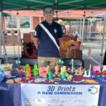 Summer company participant 3D prints at a market booth